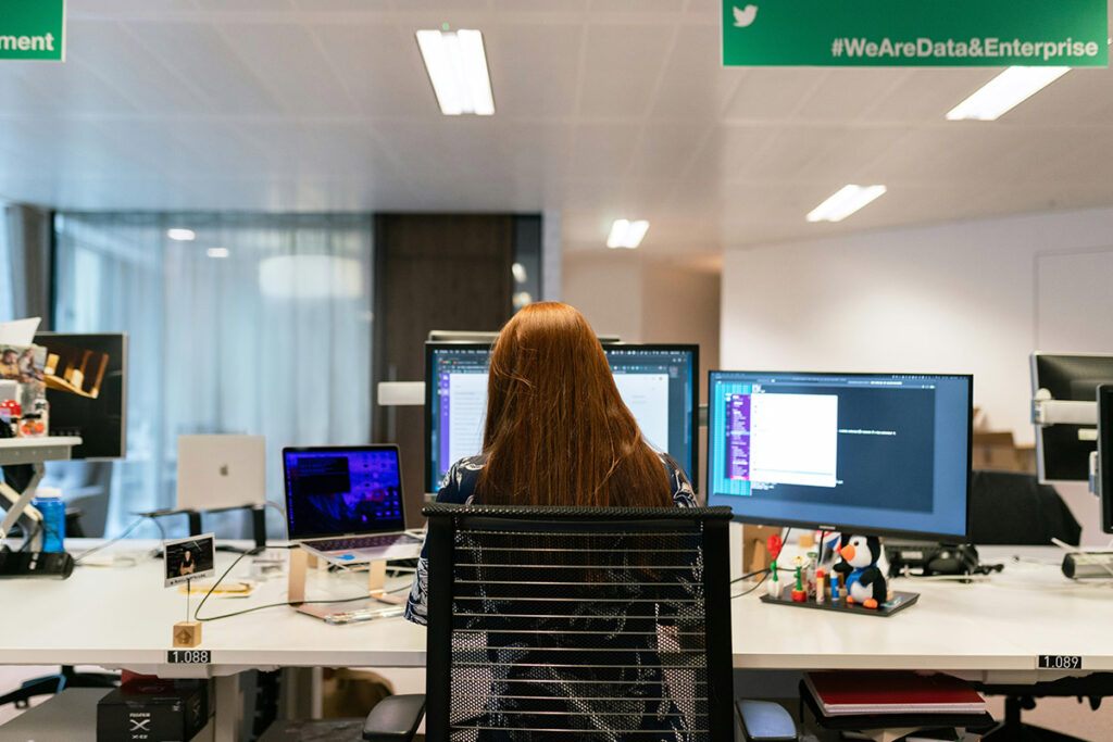 Woman sitting at desk working with multiple monitors in front of her.