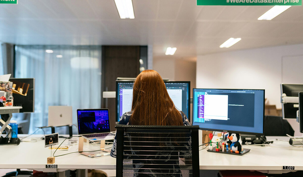 Woman sitting at desk working with multiple monitors in front of her.