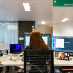 Woman sitting at desk working with multiple monitors in front of her.